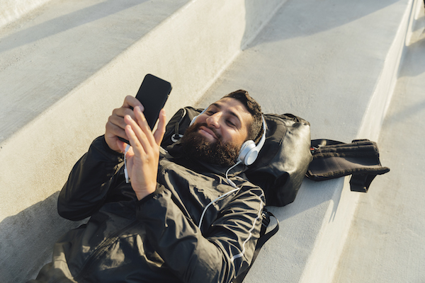 Man lying on steps playing with smart phone and using headphones