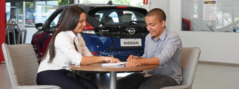 pessoas sentadas ao redor de um computador com a imagem de um carro